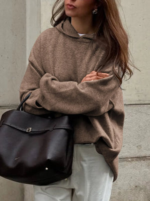 Person wearing a brown sweater holding a black bag against a neutral background