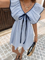 Woman wearing a blue and white striped dress with ruffled sleeves on a cobblestone street.