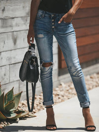 Person wearing ripped blue jeans and holding a black handbag outdoors.