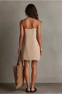 Woman wearing a beige dress holding a woven bag against a plain background