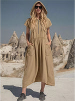 Woman wearing a beige hooded dress in a desert landscape with rock formations.