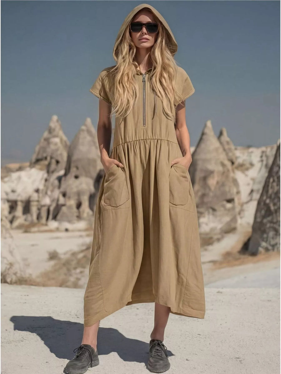 Woman wearing a beige hooded dress in a desert landscape with rock formations.