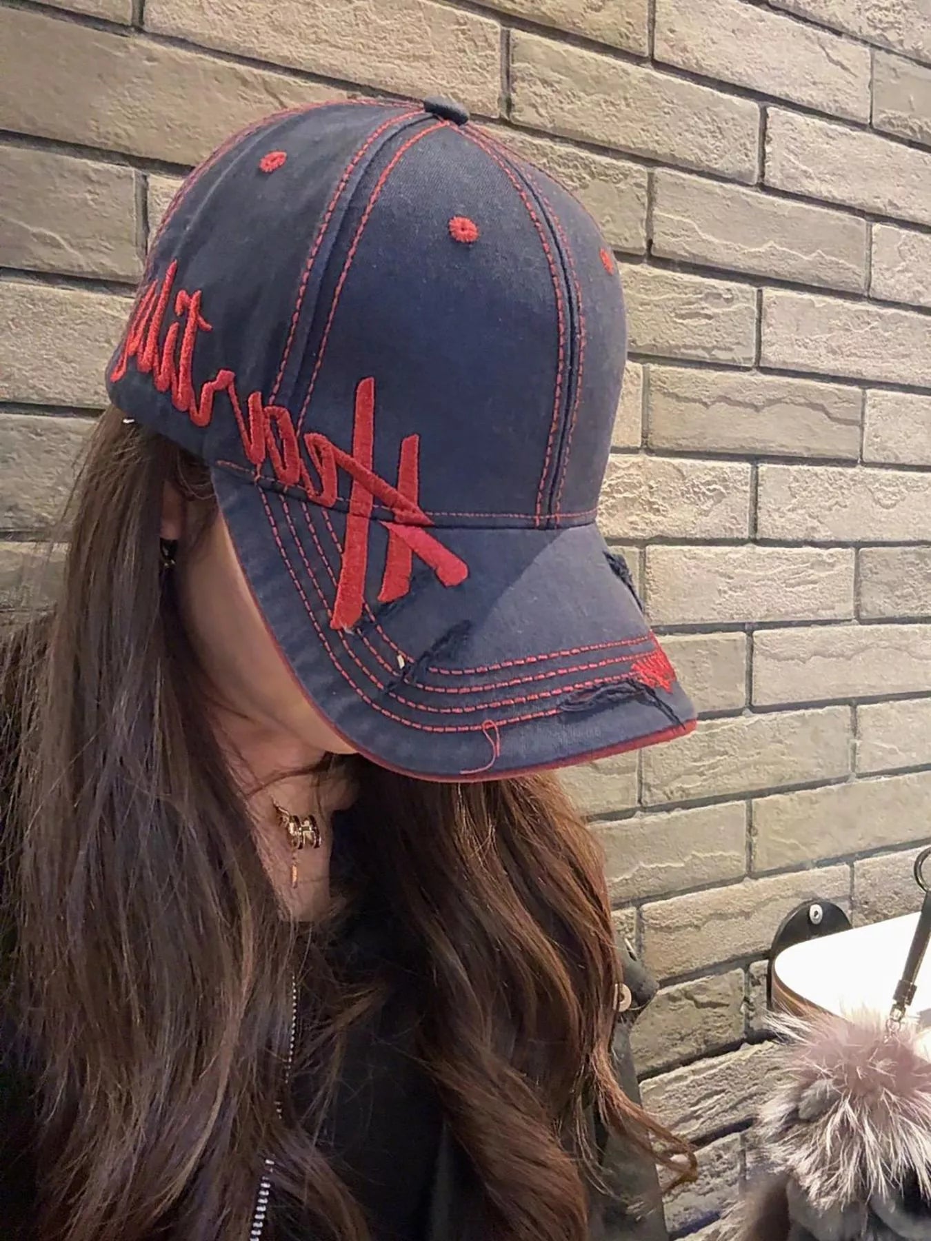 Person wearing a navy blue cap with red text against a brick wall.