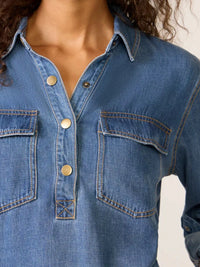 Close-up of a blue denim shirt with buttons and pockets on a neutral background