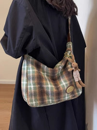 Plaid handbag with a plush toy attached, worn by a person in a dark outfit.