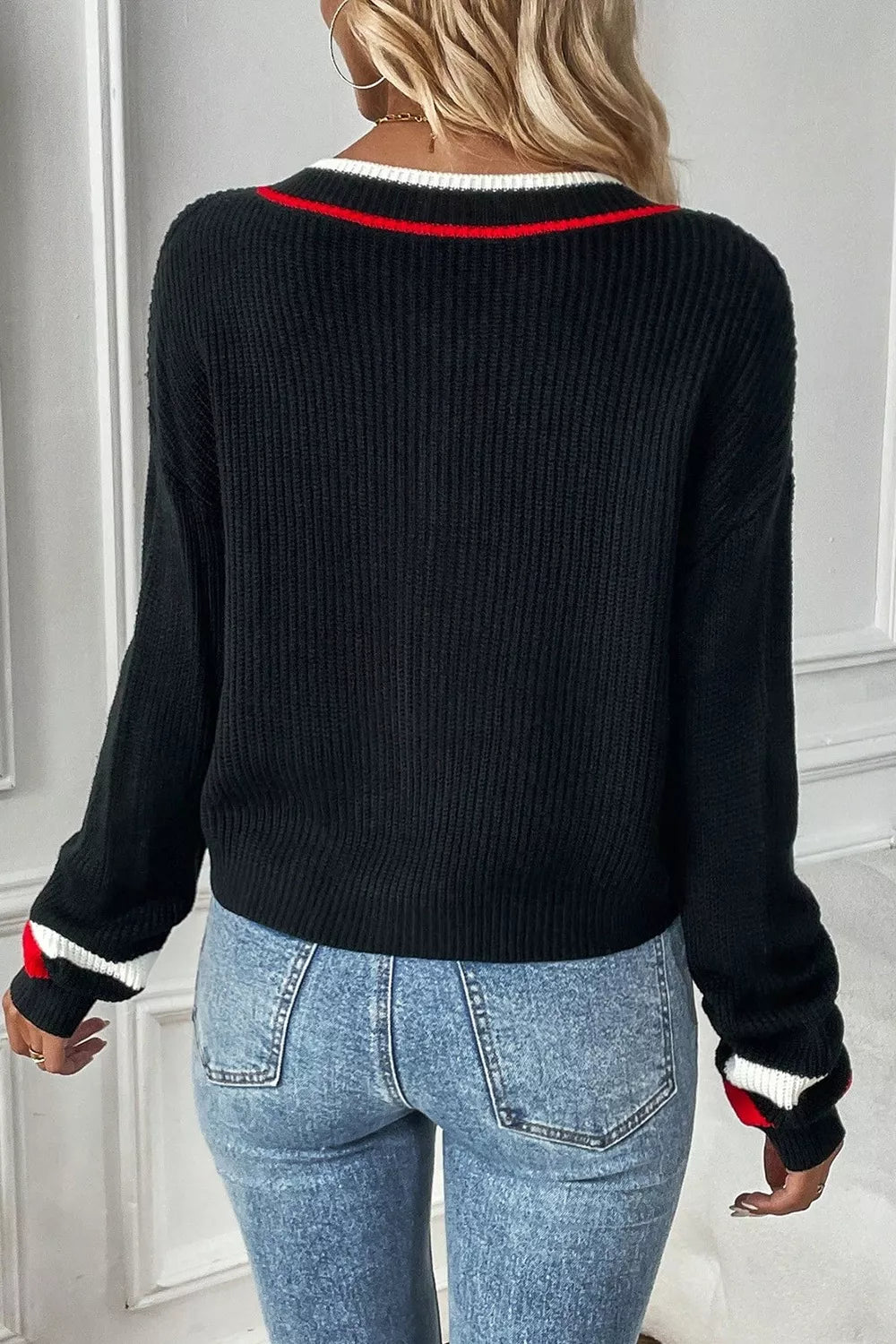 Person wearing a black sweater with red and white accents and blue jeans.