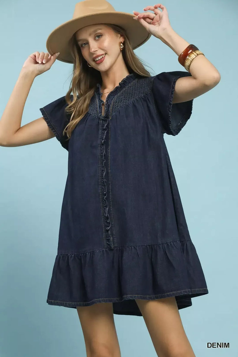 Woman wearing a denim dress and hat against a light blue background