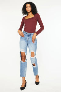 Woman wearing a burgundy long-sleeve top and ripped blue jeans on a white background