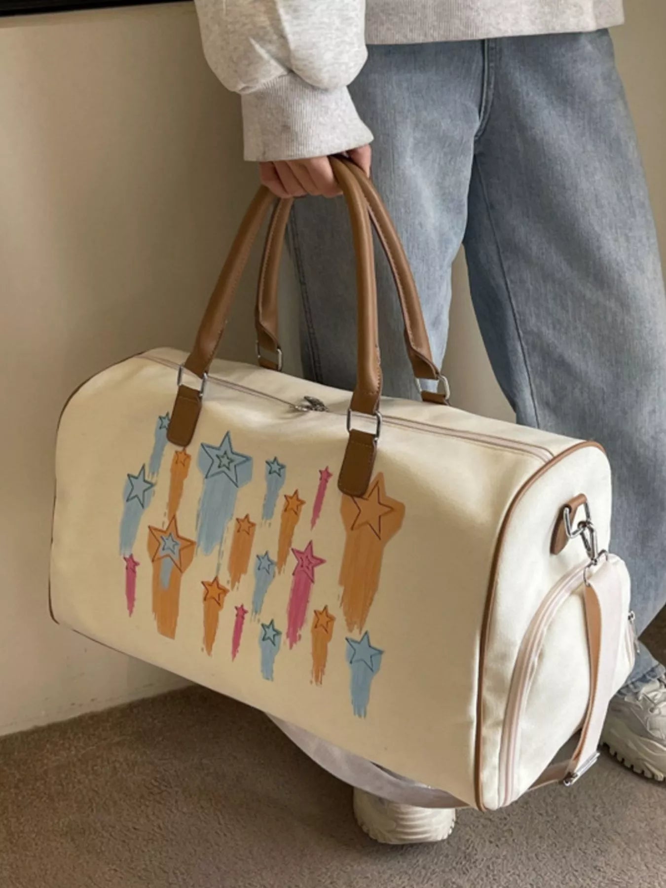 Person holding a beige duffel bag with star designs against a neutral background