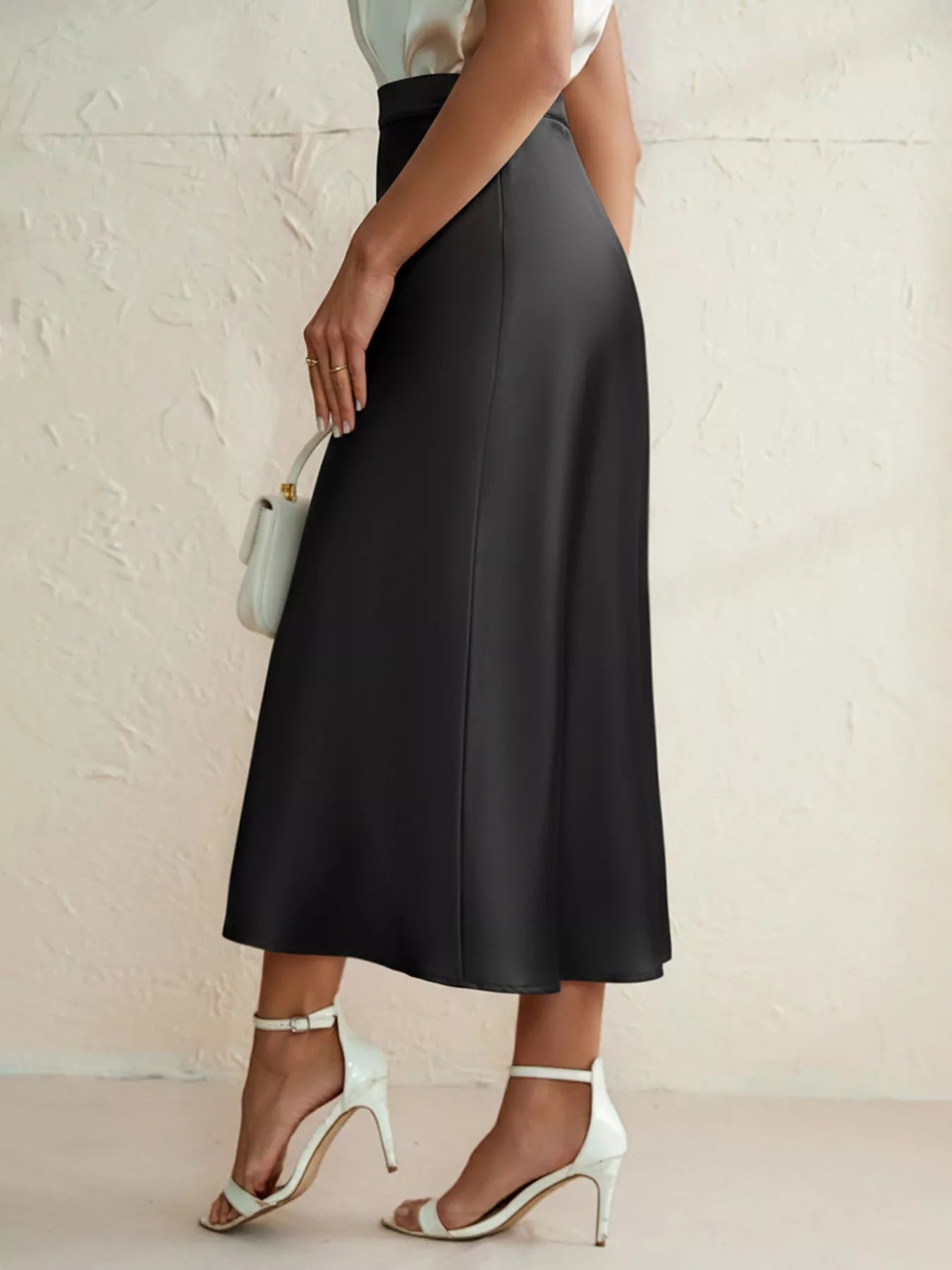 Person wearing a black skirt with white shoes and a small handbag on a light background