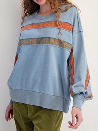 Person wearing a blue sweatshirt with orange and green patterns on a white background
