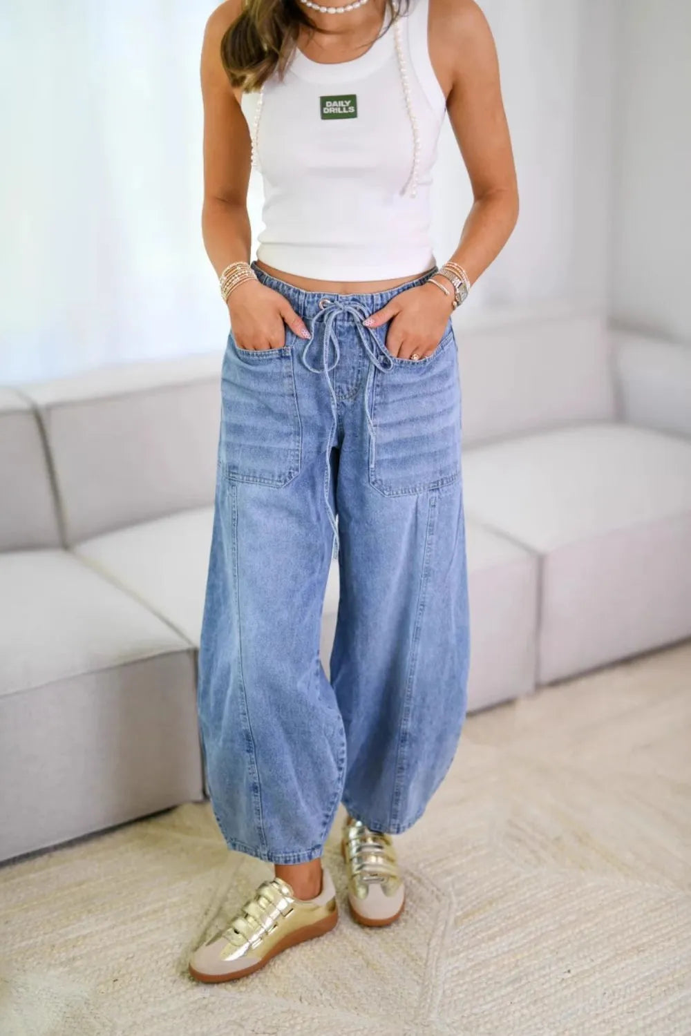 Person wearing a white tank top and blue jeans in a room with a white couch.