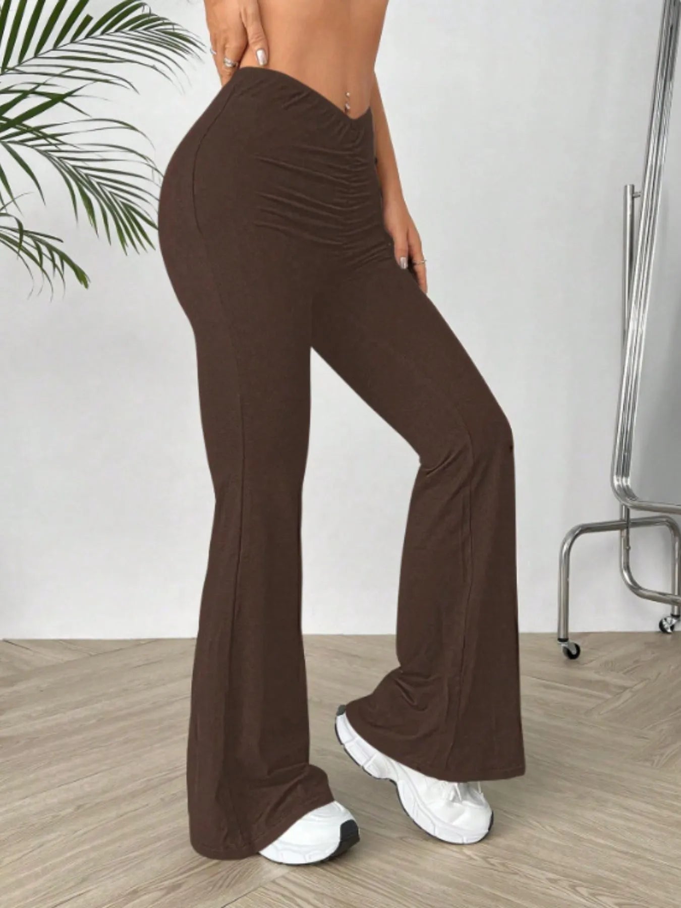 Brown flared pants worn by a person indoors with a white wall and wooden floor.