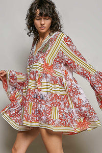 Woman wearing a colorful floral dress with long sleeves against a neutral background