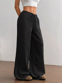 Person wearing black wide-leg pants with a plain background