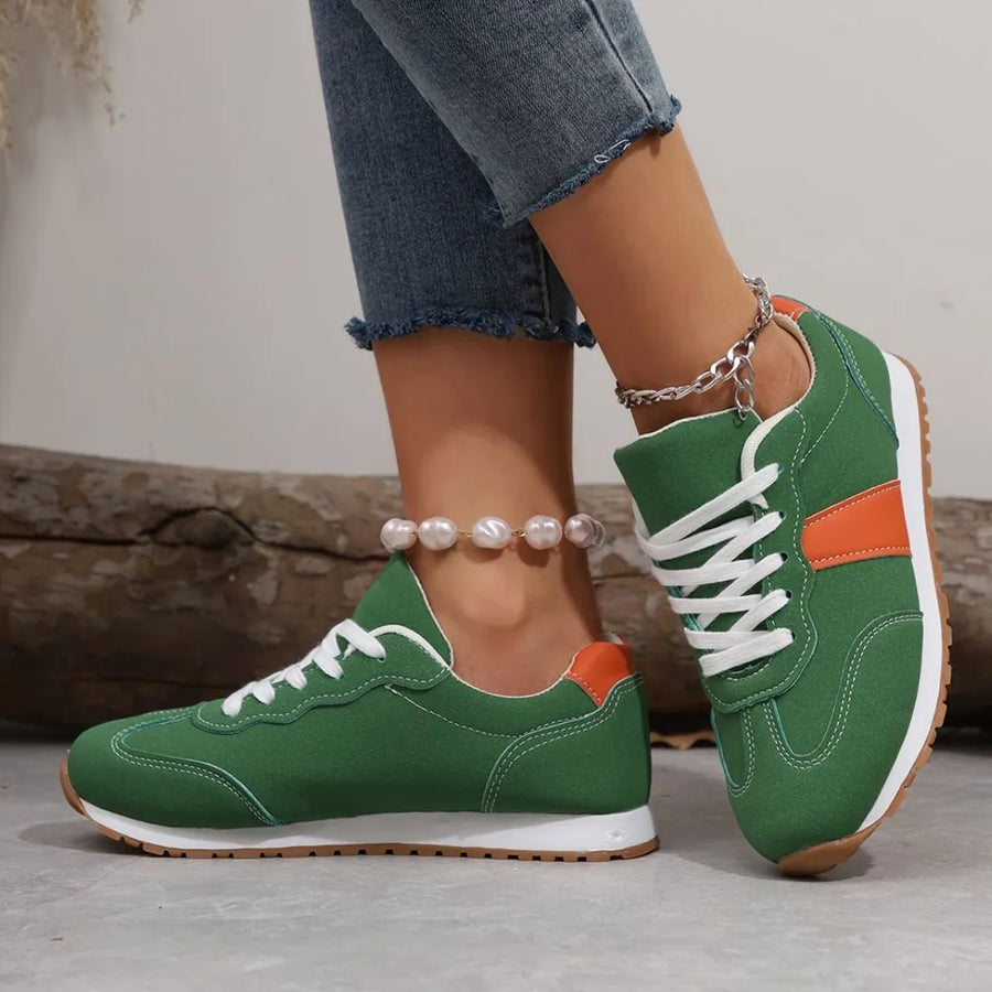 Green sneakers with orange accents worn by a person on a neutral background
