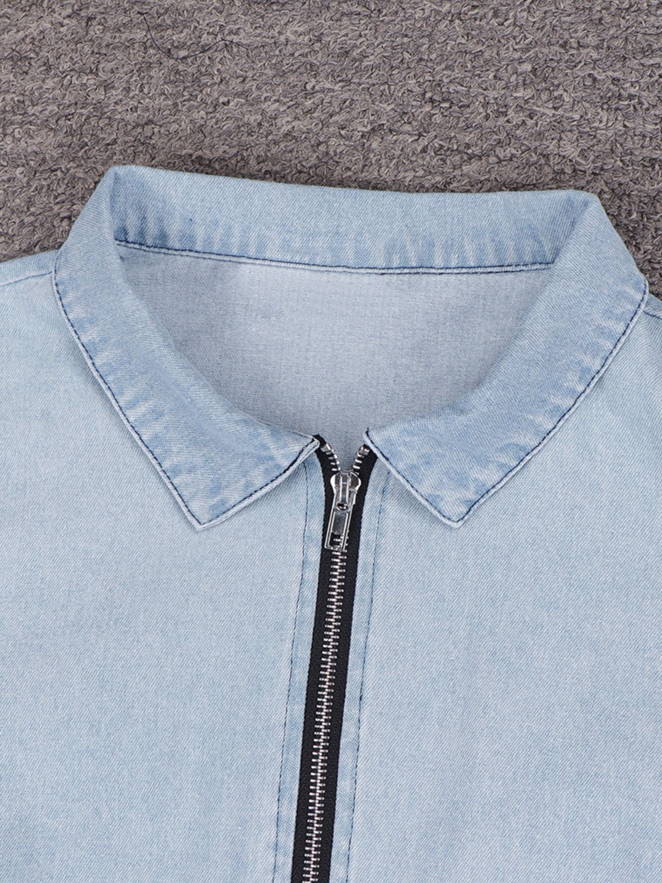 Light blue denim jacket with a zipper on a gray background
