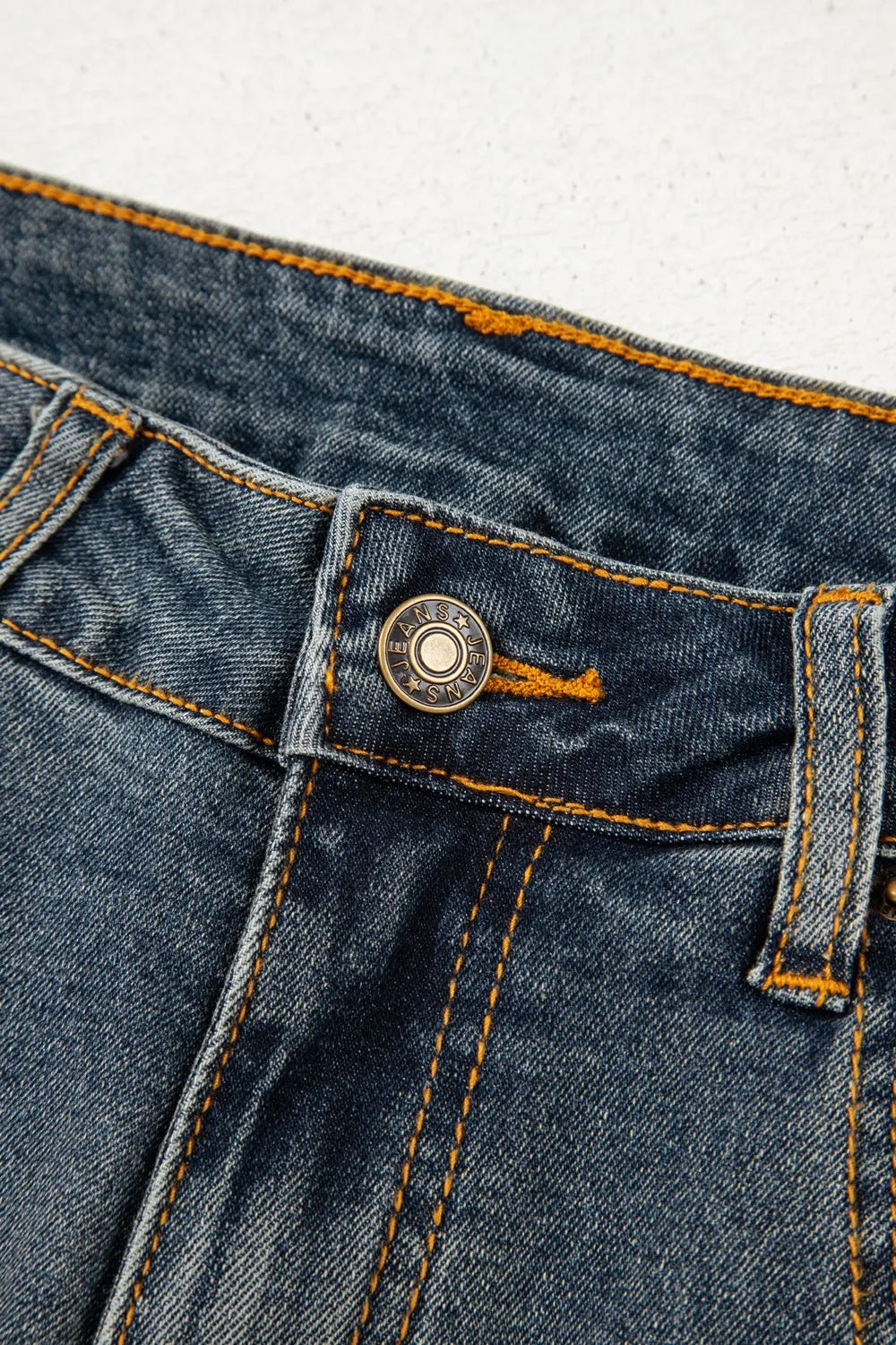 Close-up of a blue denim button and stitching detail on a light gray background