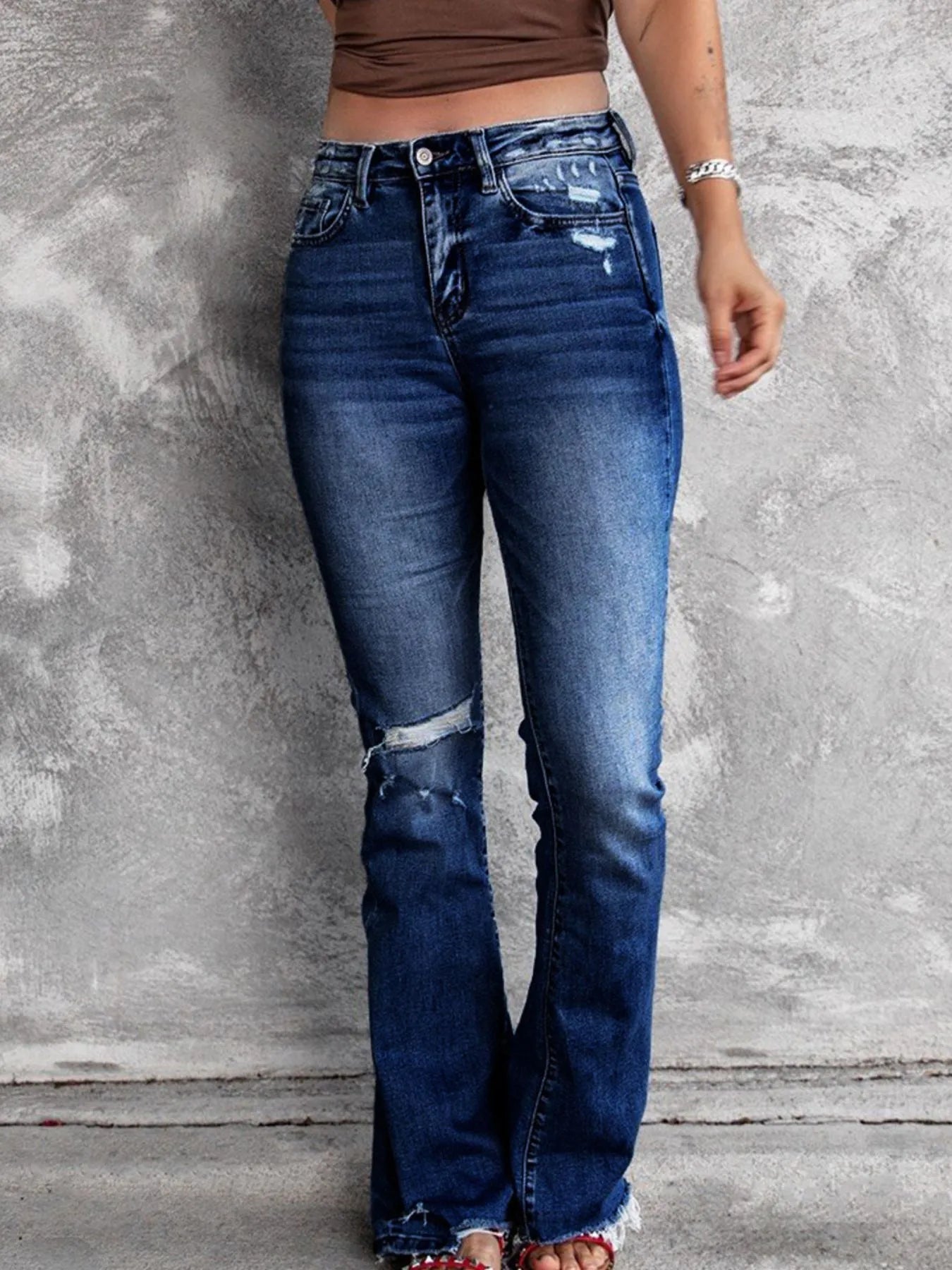 Person wearing blue jeans with a distressed design against a gray concrete wall.