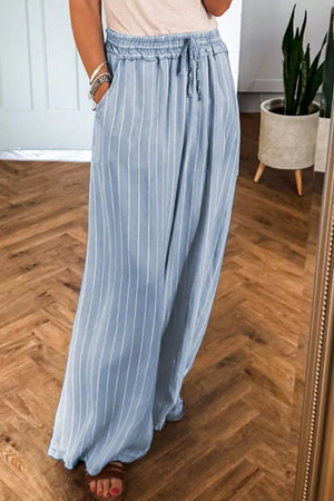 Person wearing light blue striped pants standing on a wooden floor.