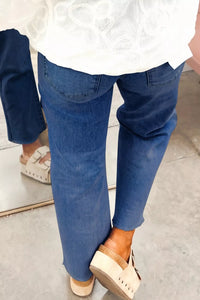 Person wearing blue jeans and white lace top with beige sandals on a neutral background