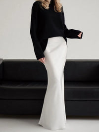 Person wearing a black sweater and white pants standing in front of a black couch.