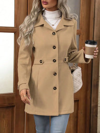 Woman wearing a beige coat holding a coffee cup in front of a wooden door.