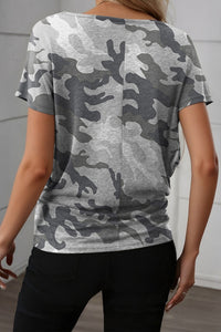 Person wearing a gray camouflage t-shirt against a white wall.