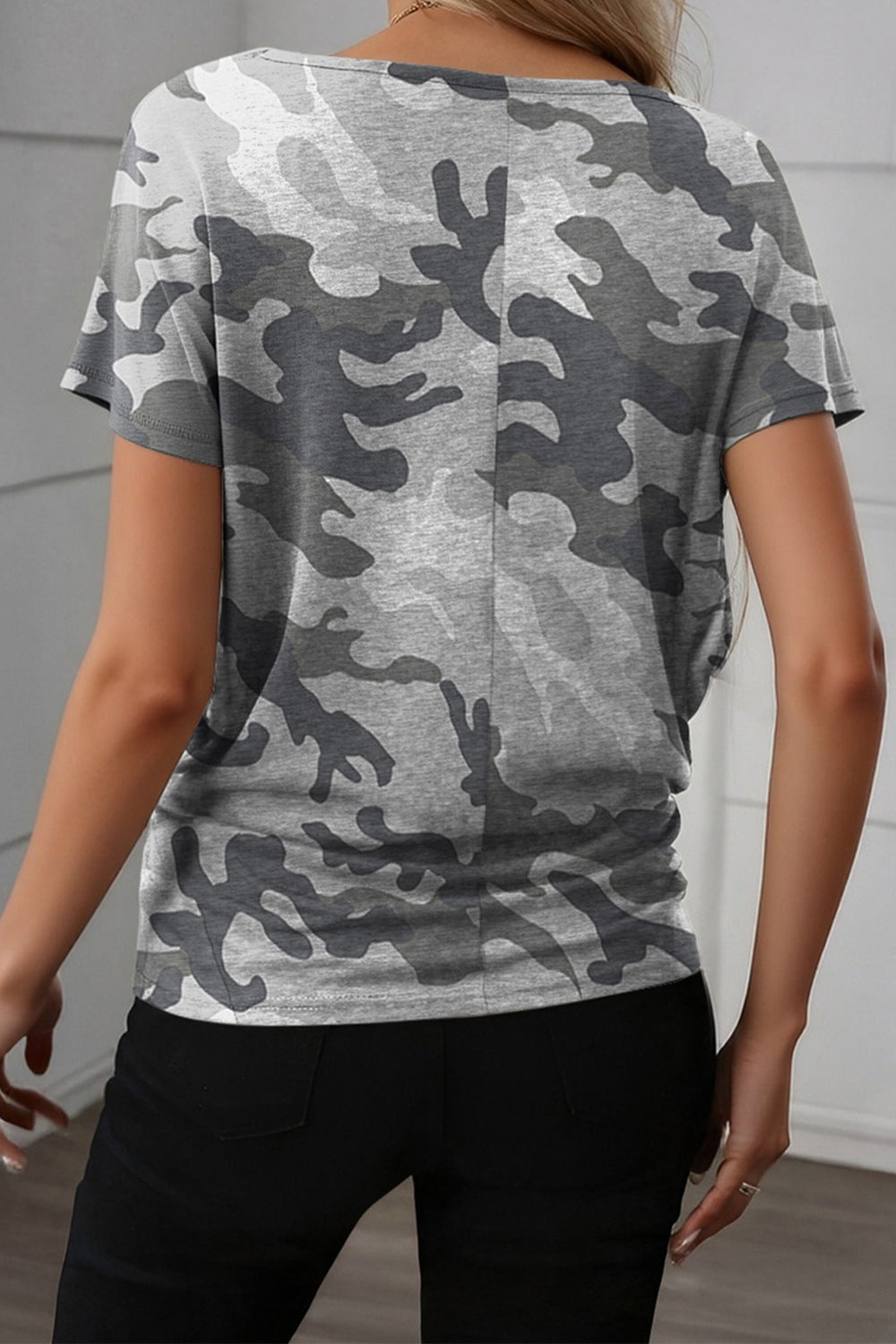 Person wearing a gray camouflage t-shirt against a white wall.