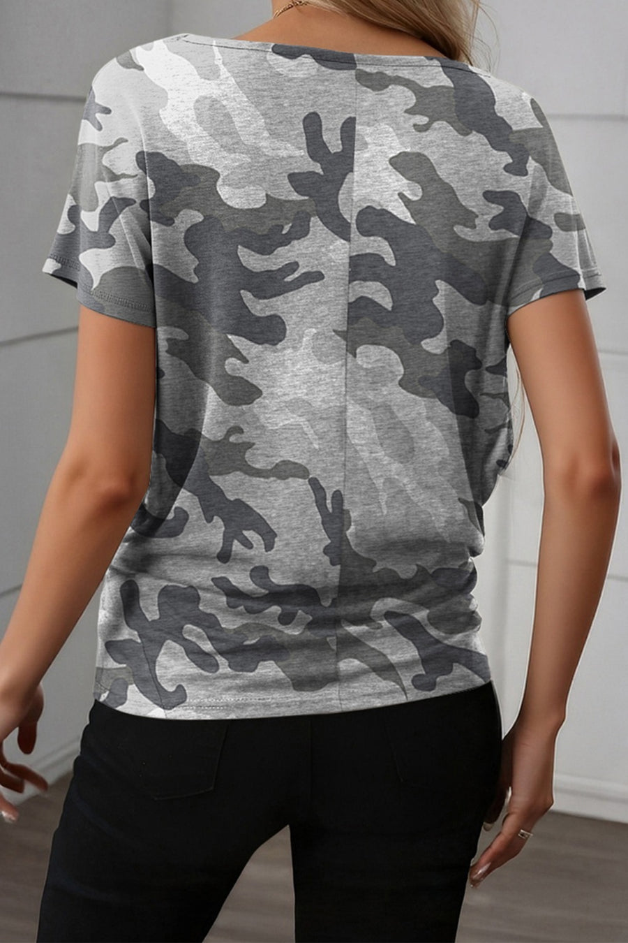 Person wearing a gray camouflage t-shirt against a white wall.