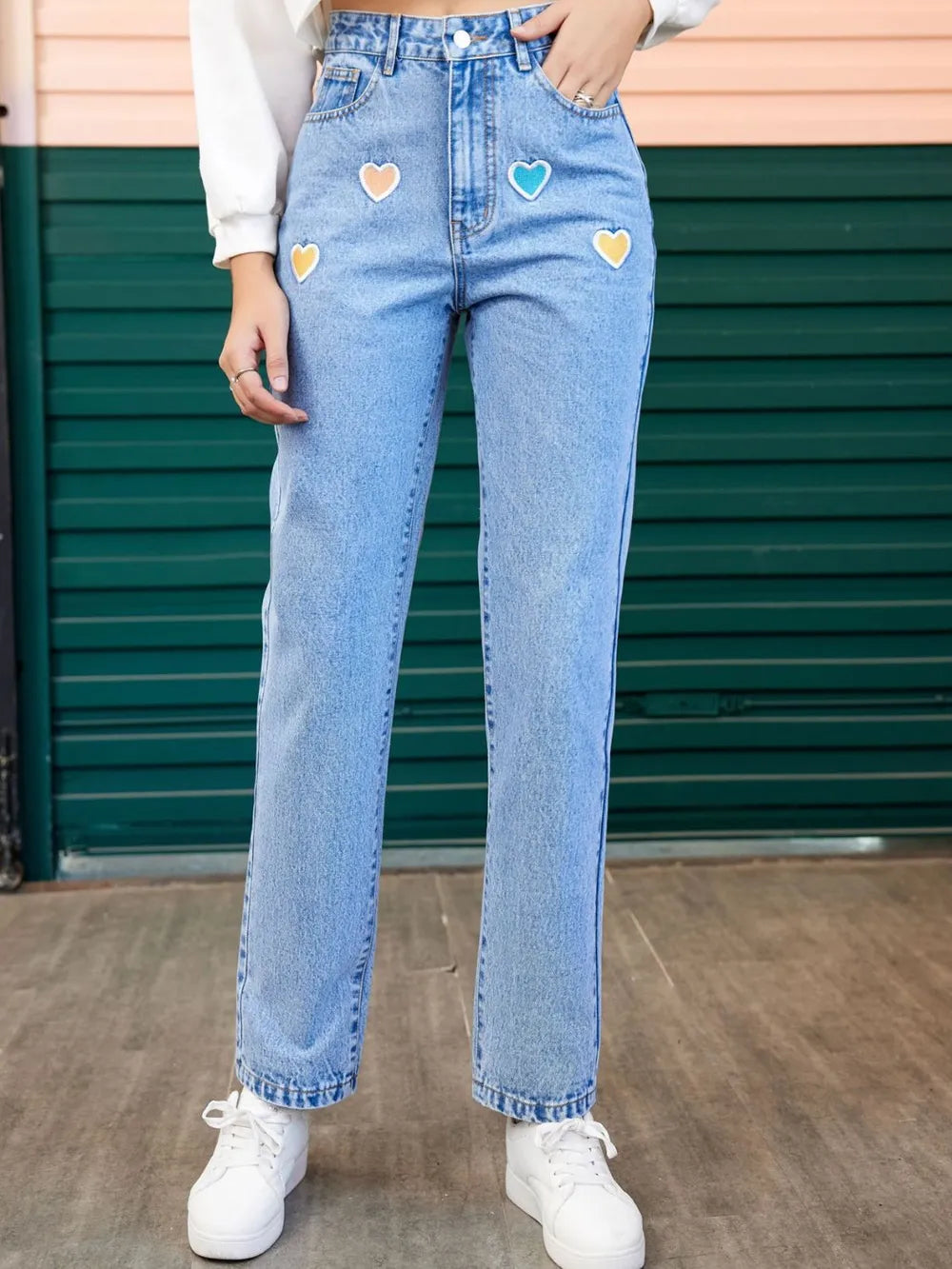 Person wearing light blue jeans with colorful heart patches in front of a green door.