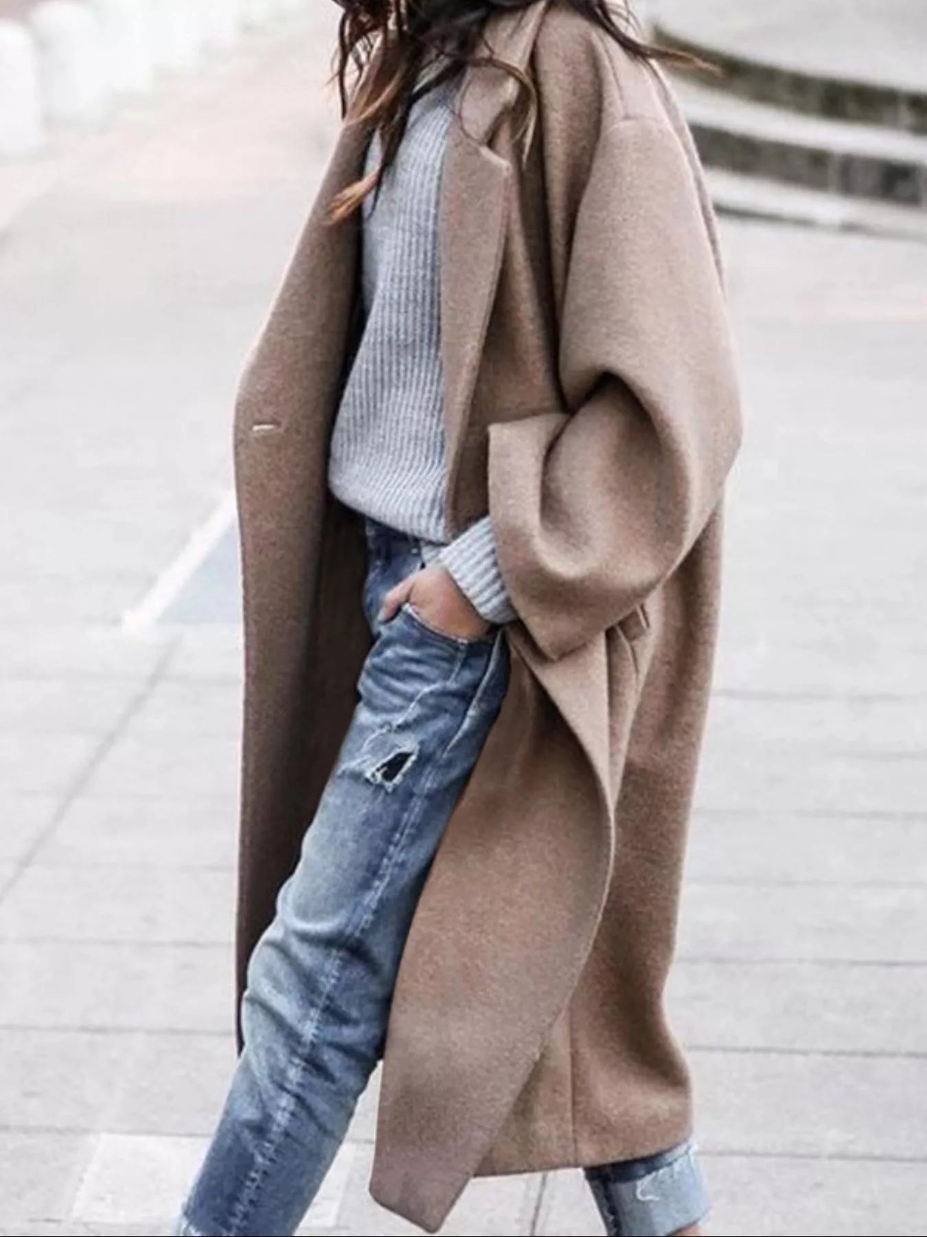 Person wearing a long brown coat over a light blue sweater and jeans.