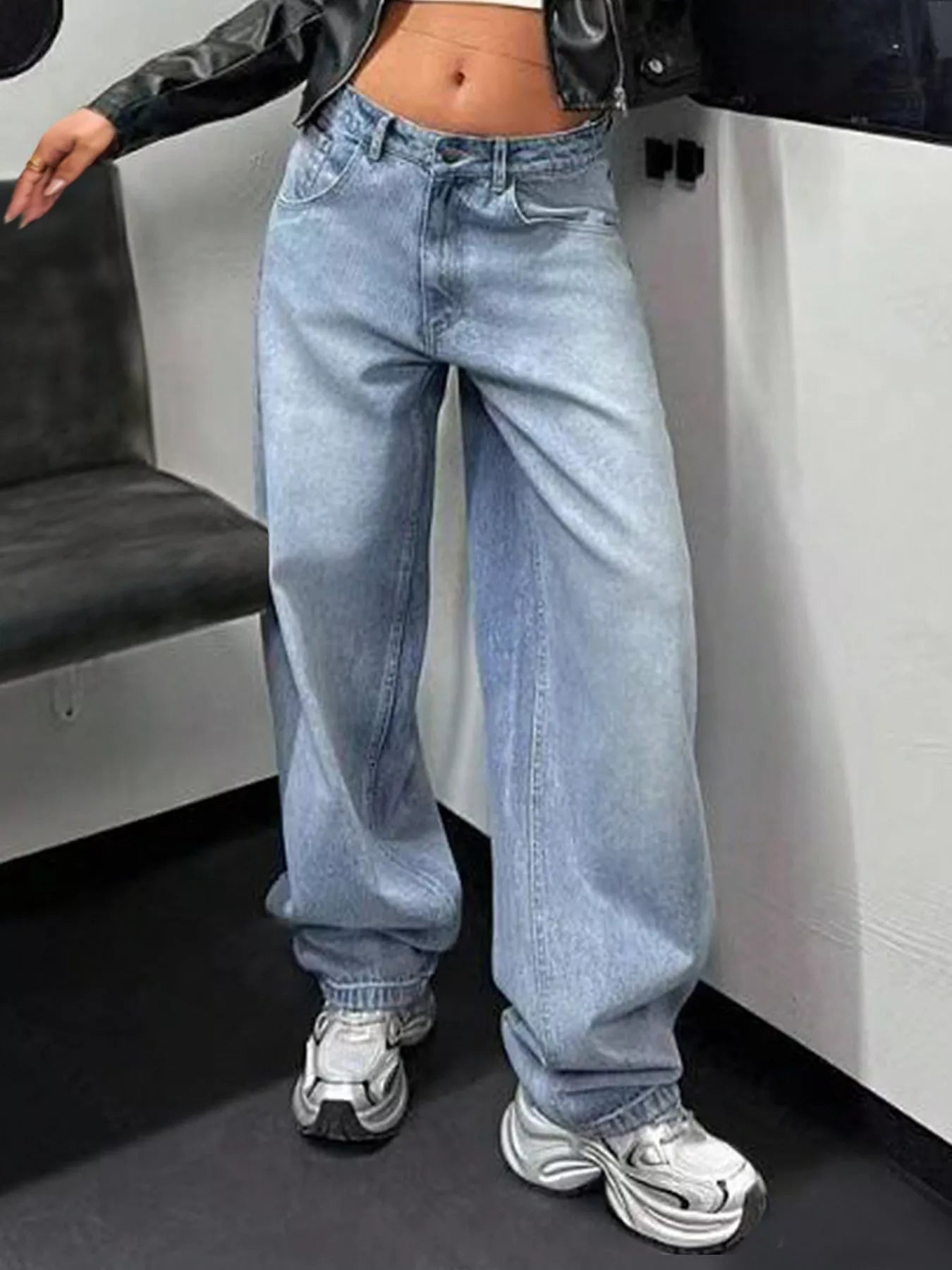 Person wearing light blue jeans and white sneakers in a minimal indoor setting