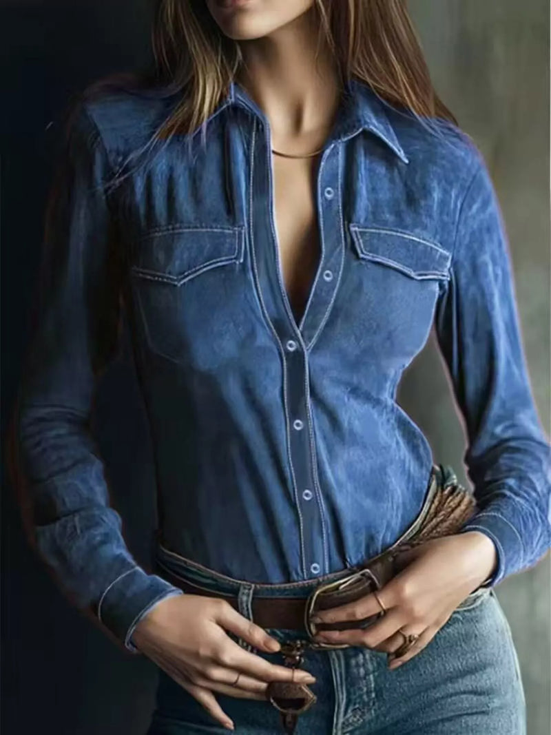 Person wearing a blue denim shirt with a deep neckline against a dark background