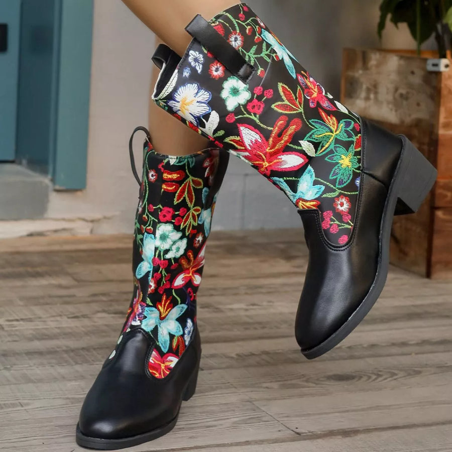 Black knee-high boots with colorful floral embroidery on a wooden floor.