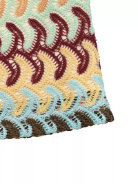 Close-up of a crocheted fabric with wavy pattern in red, yellow, and blue on a white background