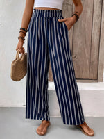 Person wearing navy and white striped pants with a white top and brown sandals, holding a woven bag.