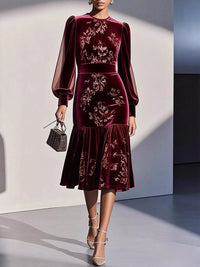 Woman wearing a burgundy velvet dress with floral embroidery against a neutral background