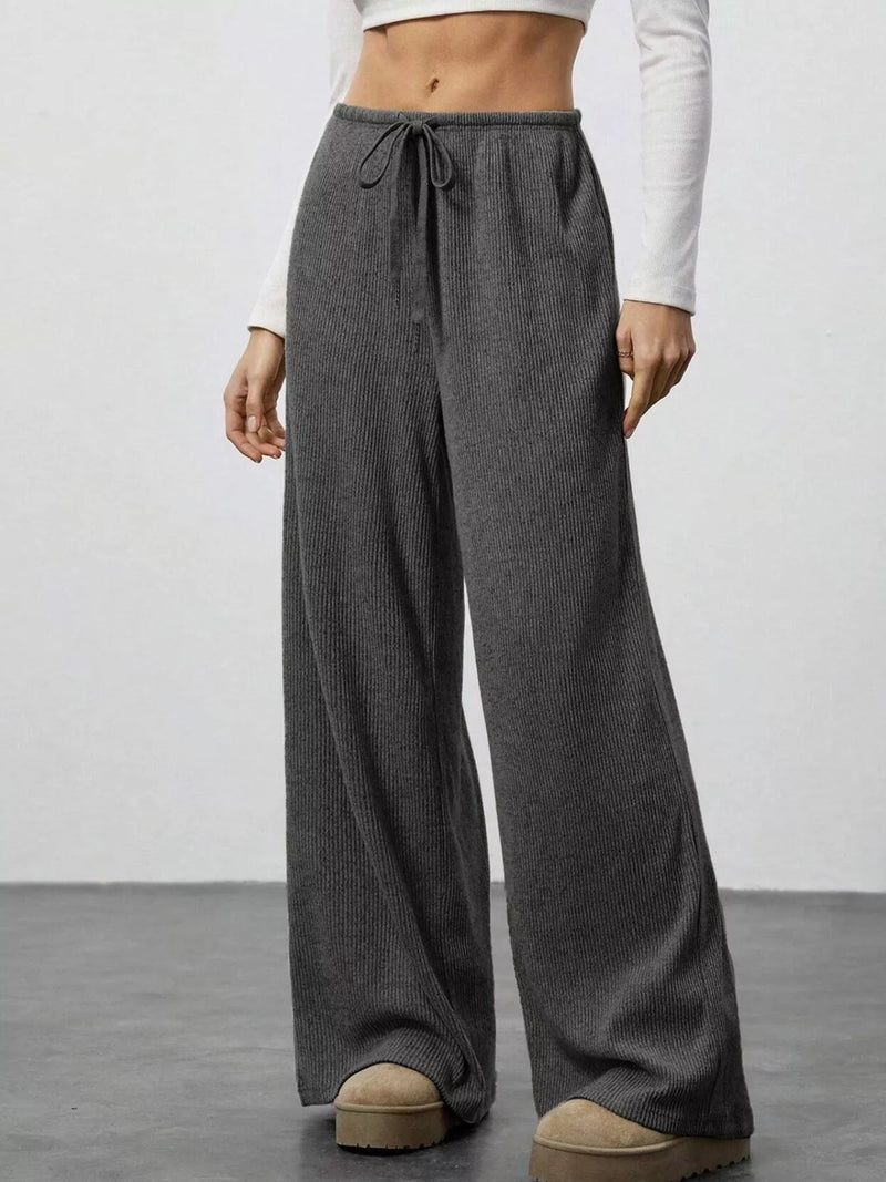 Person wearing gray wide-leg pants with a white top on a plain background