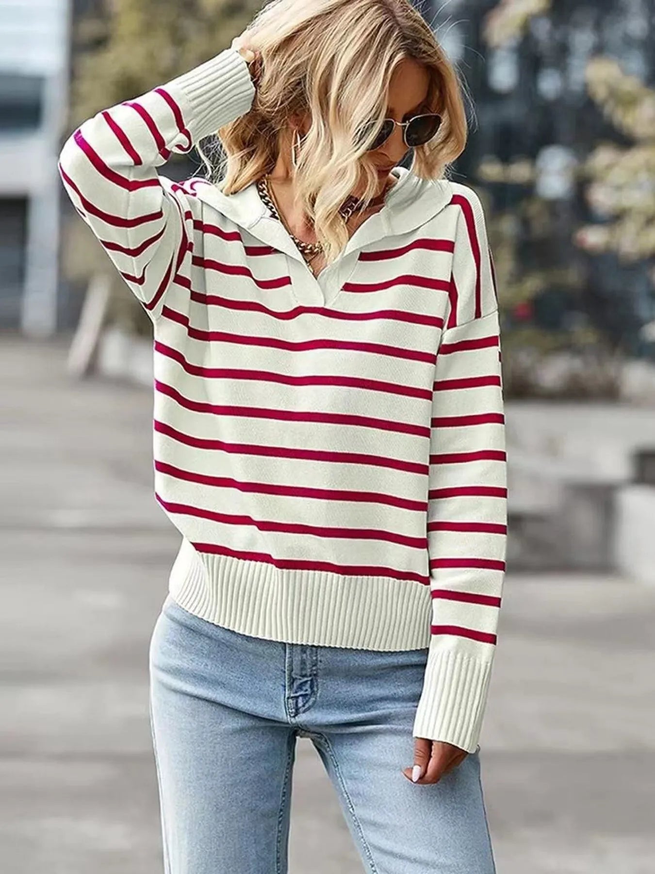 Person wearing a red and white striped sweater with light blue jeans outdoors.