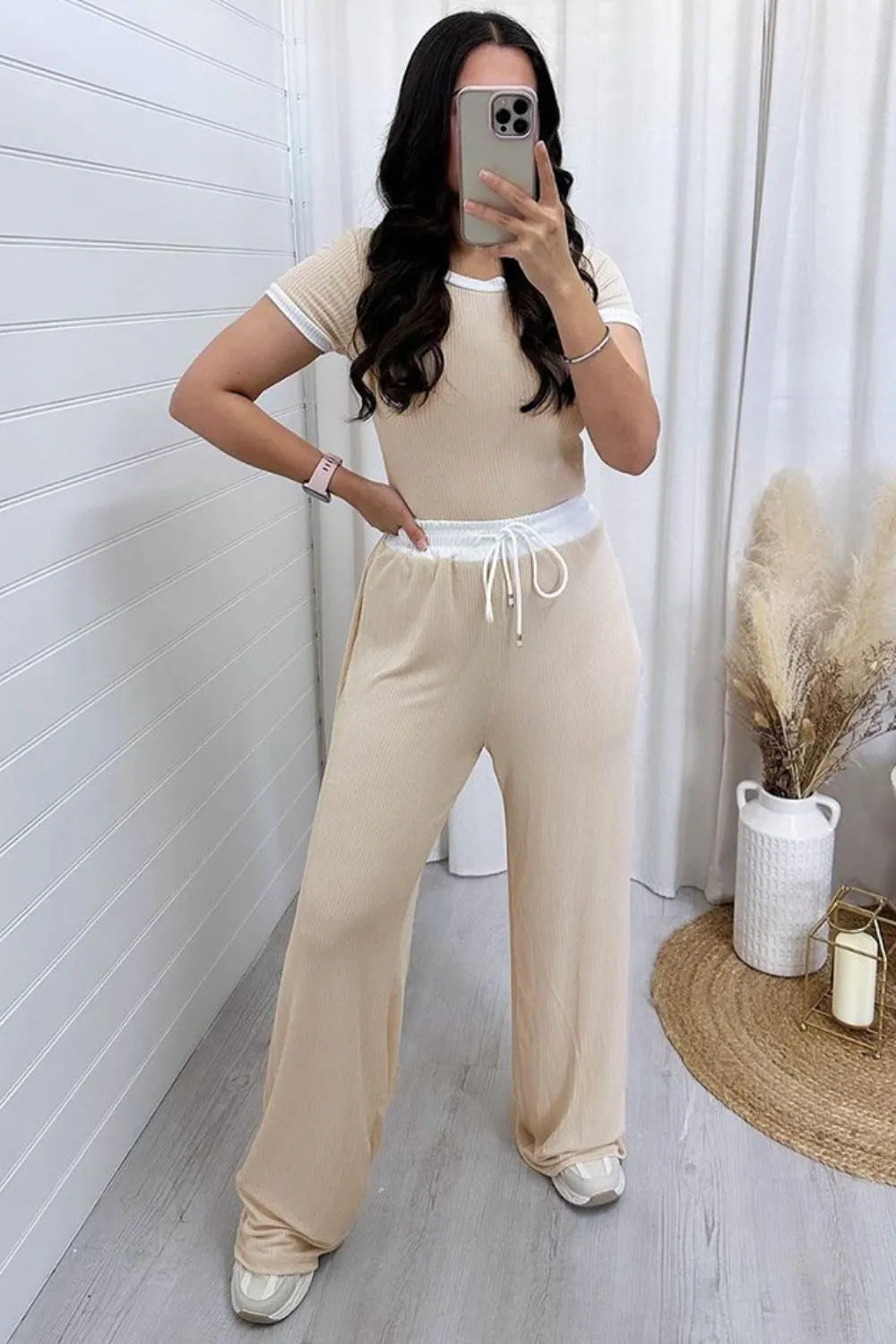 Woman taking a mirror selfie wearing a beige outfit in a minimalistic room.