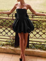 Woman wearing a black strapless dress standing on a balcony with greenery in the background