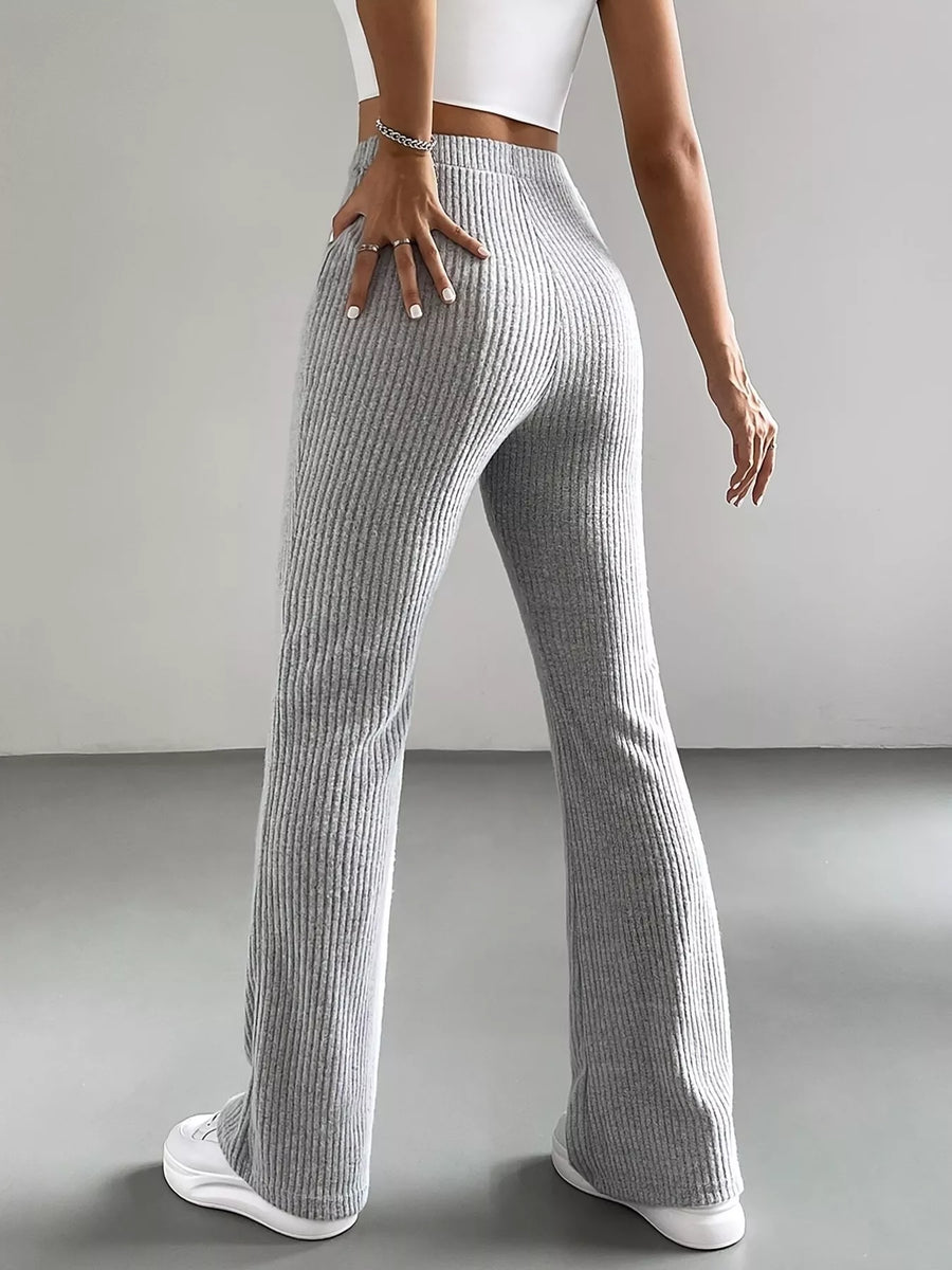Person wearing gray ribbed pants and white sneakers on a plain background