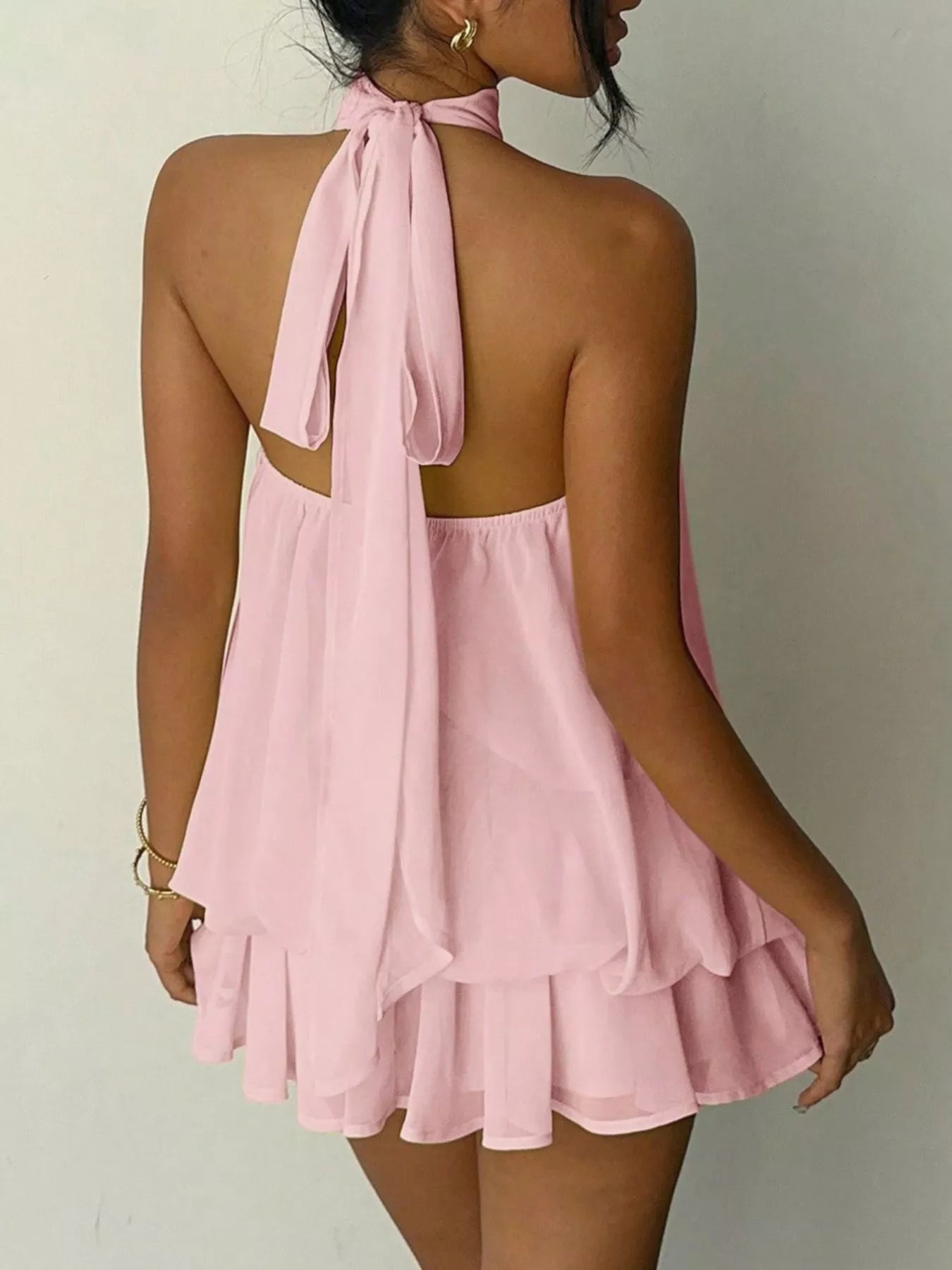 Pink halter neck dress with ruffled layers on a plain background