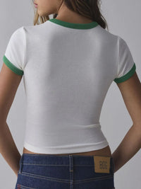 Person wearing a white crop top with green trim and blue jeans on a gray background