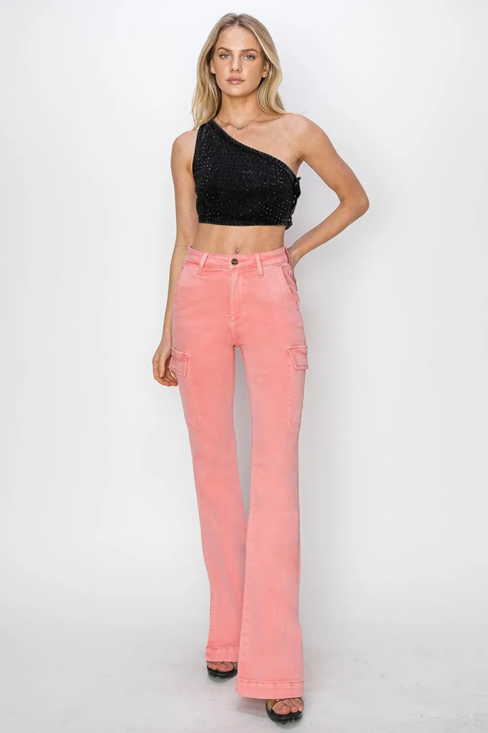 Woman wearing a black one-shoulder top and pink jeans on a white background