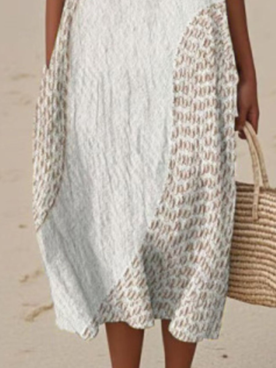 Person wearing a textured white dress holding a straw bag on a beach.