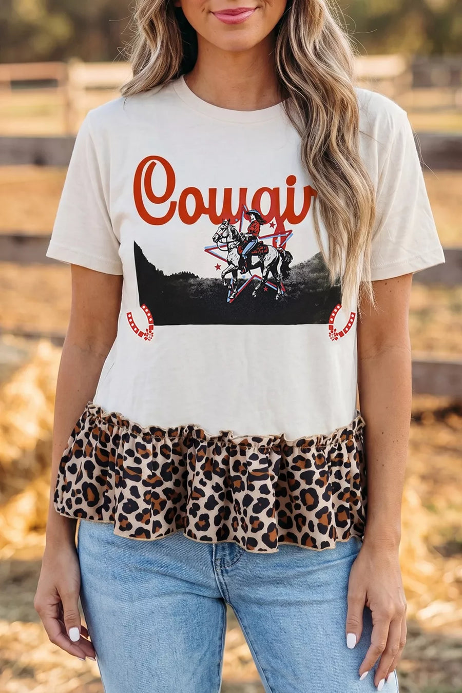 Person wearing a white t-shirt with 'Cowgirl' graphic and leopard print hem, standing outdoors.
