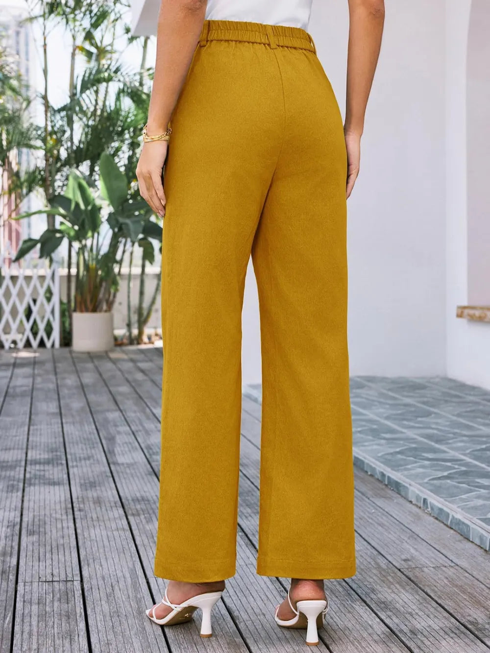 Mustard yellow wide-leg pants worn by a person on a wooden deck.