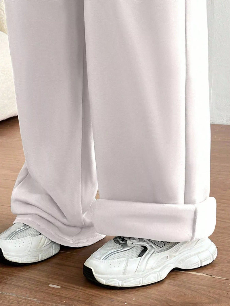 White pants with a slight crease worn by a person on a wooden floor.